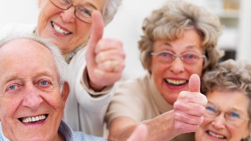 Gruppe alter Menschen lacht in Kamera, zeigen Daumen nach oben