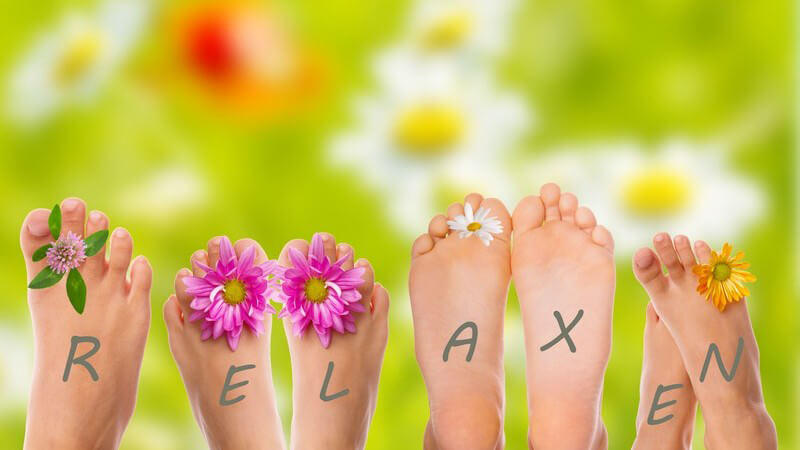 Entspannen und Füße hochlegen: Nackte Füße, darauf Blumen und das Wort "Relaxen"