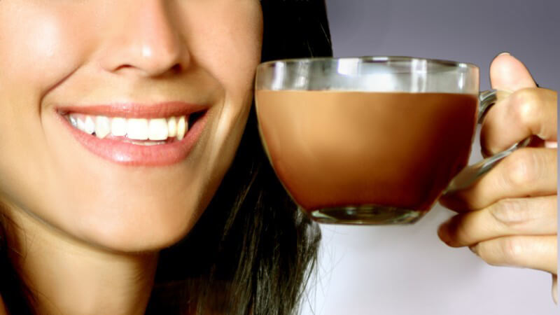 Glastasse mit Kakao, lächelnde frau hält sie auf Höhe des Mundes