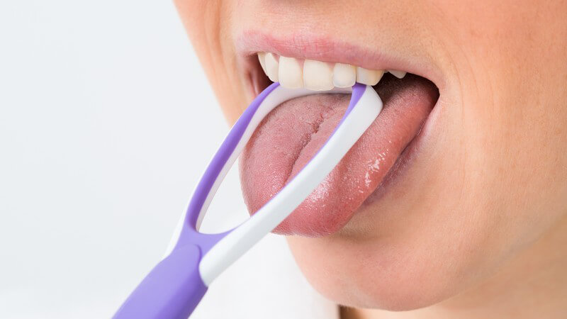 Frau reinigt ihre Zunge mit einem lila Zungenreiniger