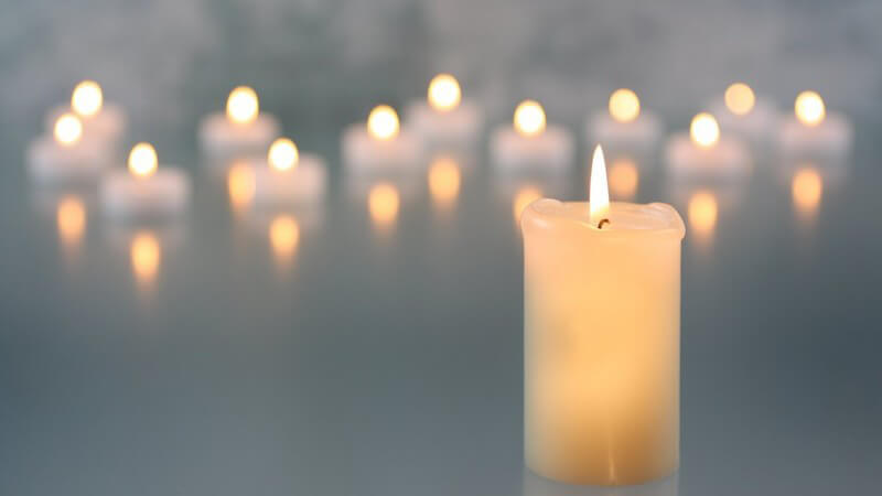 Weiße brennende Kerze, im Hintergrund viele Kerzenlichter