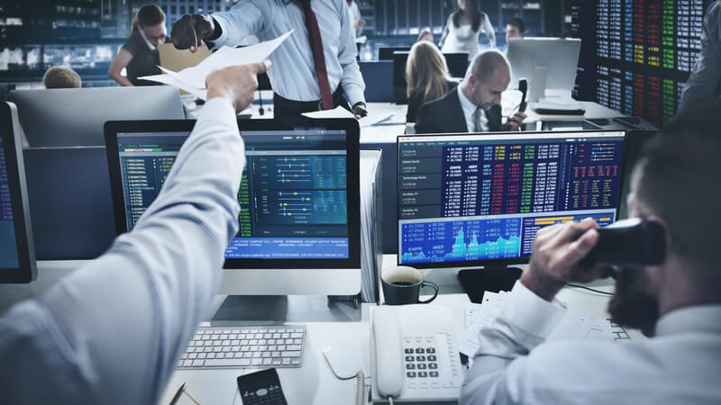 Trader sitzen an der Börse vor ihren Computern, einer reicht ein paar Zettel weiter
