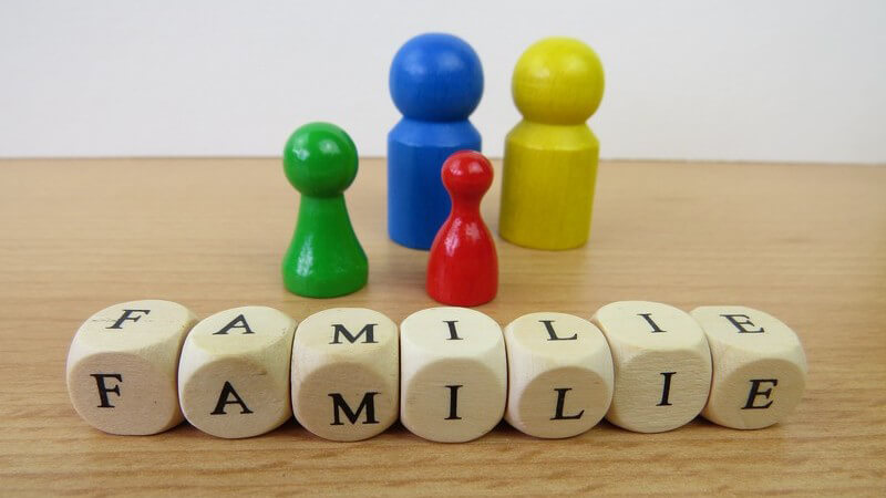 Buchstabenwürfel bilden das Wort "Familie" auf einem Holztisch vor vier farbigen Brettspielfiguren