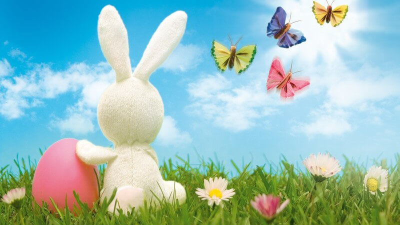 Grafik zu Ostern - Weißer Hase neben rosa Osterei auf Blumenwiese und Schmetterlinge am blauen Himmel