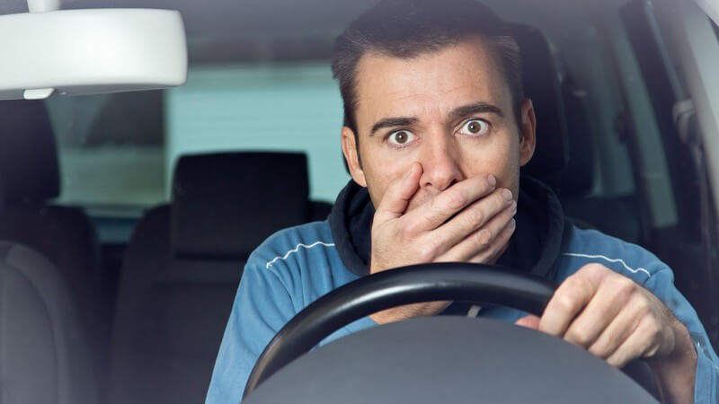 Junger Autofahrer hinter dem Lenkrad, hält sich unter Schock die Hand vor den Mund