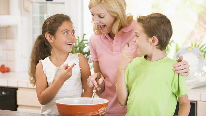 Mutter mit ihren beiden Kindern in Küche beim Backen, Mädchen probiert Teig