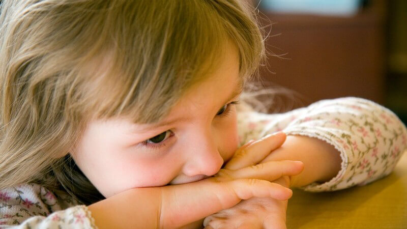 Kleines Mädchen mit Armen auf Tisch stützt Gesicht auf Hände