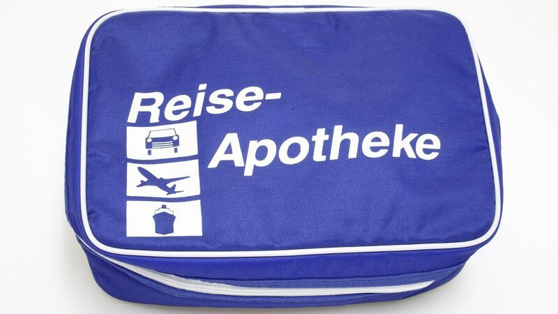 Blaue Tasche mit Schrift "Reise-Apotheke" und Bildern von Auto, Flugzeug und Schiff