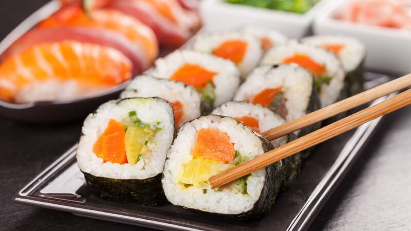 Essstäbchen greifen ein Stück Sushi von einer kleinen Sushi-Platte