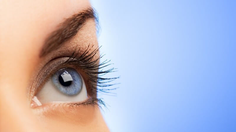 Linkes Auge einer Frau, sie schaut nach oben, hellblauer Hintergrund