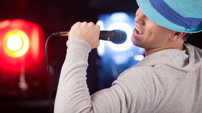 Mann in grauem Sweatshirt und blauem Hut singt in ein Mikrofon