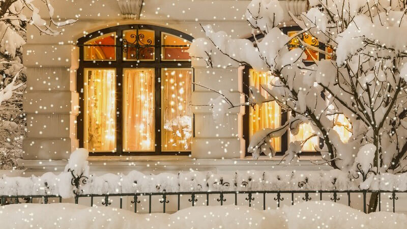 Altbau mit großen, beleuchteten Fenstern, Weihnachtsbeleuchtung, draußen Schnee, es schneit