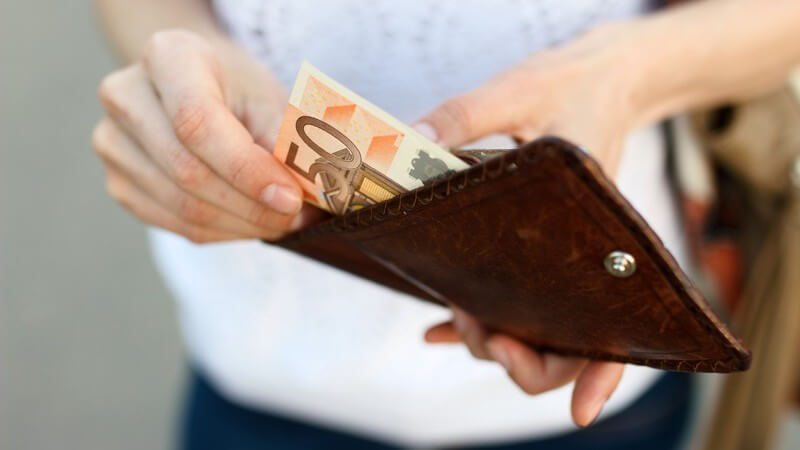 Frau nimmt einen 50-Euro-Schein aus einer braunen Geldbörse aus Leder