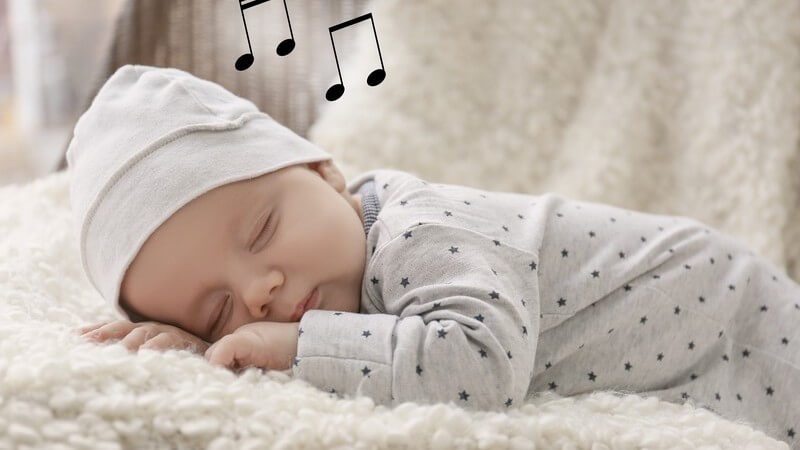 Schlafendes Baby mit Mütze auf einer Felldecke, über dem Kopf schweben Musiknoten