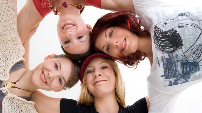 4 Frauen mit unterschiedlichen Haarfarben stecken ihre Köpfe zusammen, von unten fotografiert