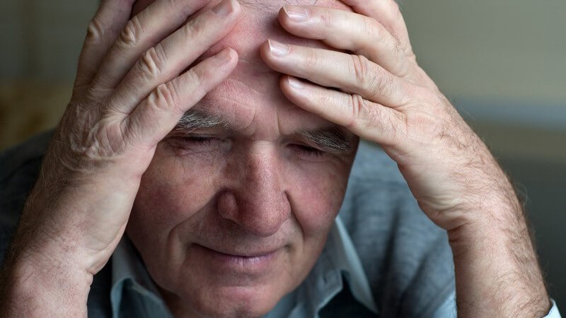 Alter Mann mit Kopfschmerzen fasst sich mit beiden Händen an die Stirn