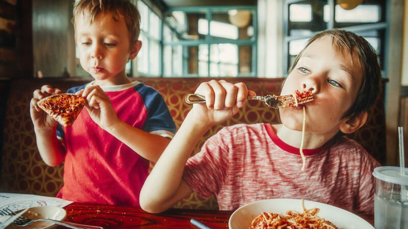 Zwei Jungen essen Pizza und Spaghetti Bolognese in einem Restaurant