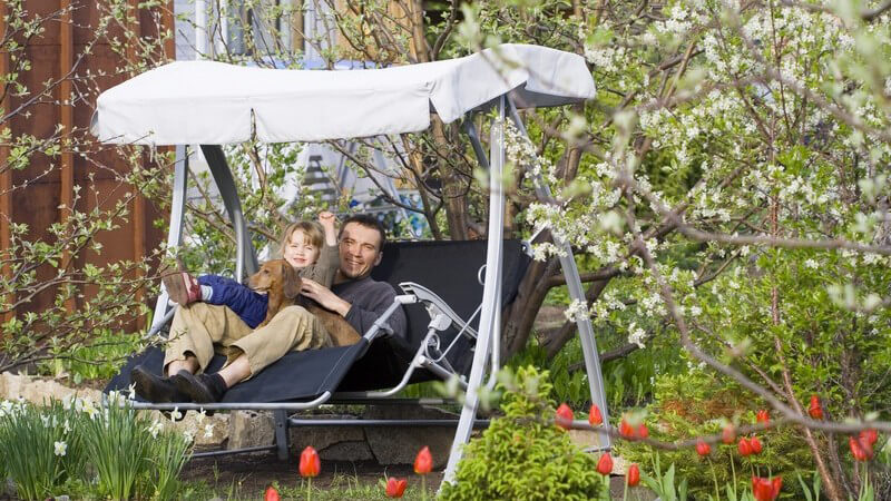 Vater mit Tochter auf Hollywood Schaukel im Garten