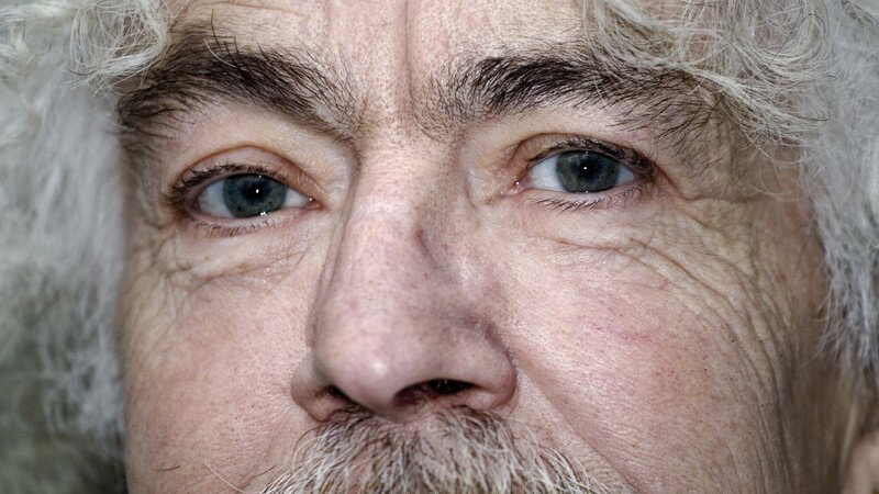 Gesichtsausschnitt eines alten Mannes mit grauen Locken und Schnurrbart