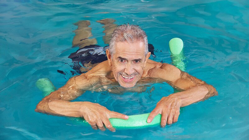 Älterer Mann mit grüner Schwimmnudel im Wasser