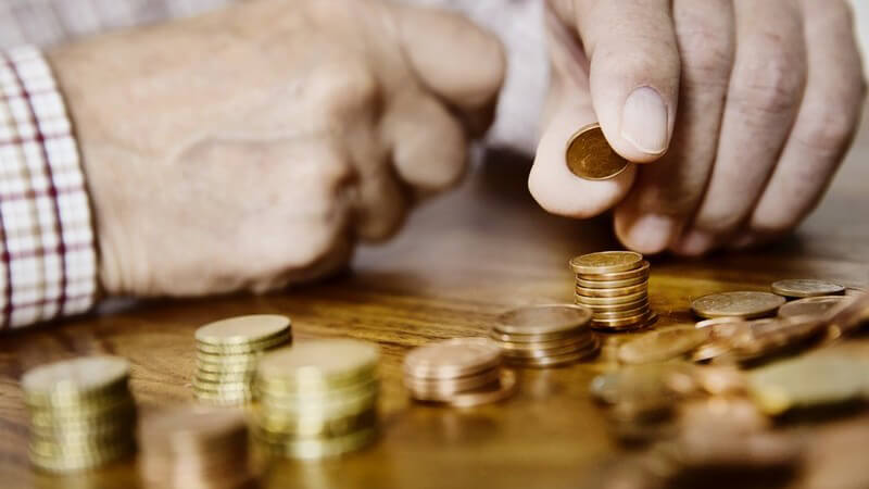 Alter Mann sortiert und zählt sein Kleingeld (Euro-Cent-Stücke) auf einem Tisch