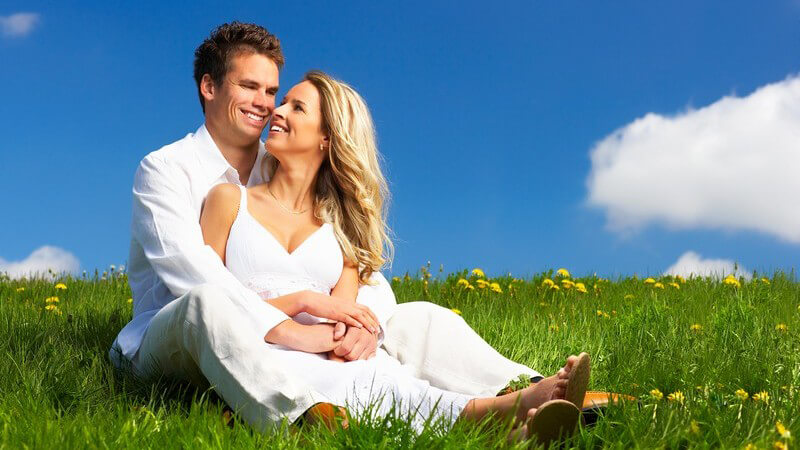 Glückliches Paar in weißer Kleidung auf Blumenwiese unter blauem Himmel