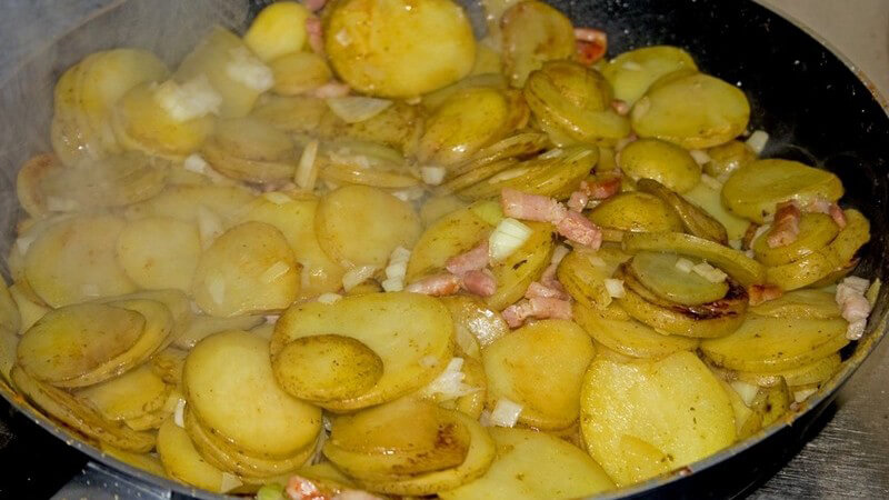 Nahaufnahme von Bratpfanne mit frischem, dampfenden Bauernfrühstück, Bratkartoffeln, Zwiebeln, Speck