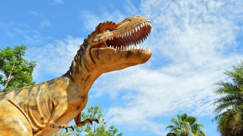 Dinosaurier-Modell unter blauem Himmel und Palmen