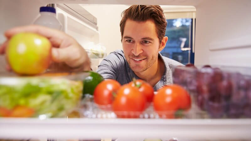 Mann nimmt einen Apfel aus einem Kühlschrank voller gesunder Nahrungsmittel