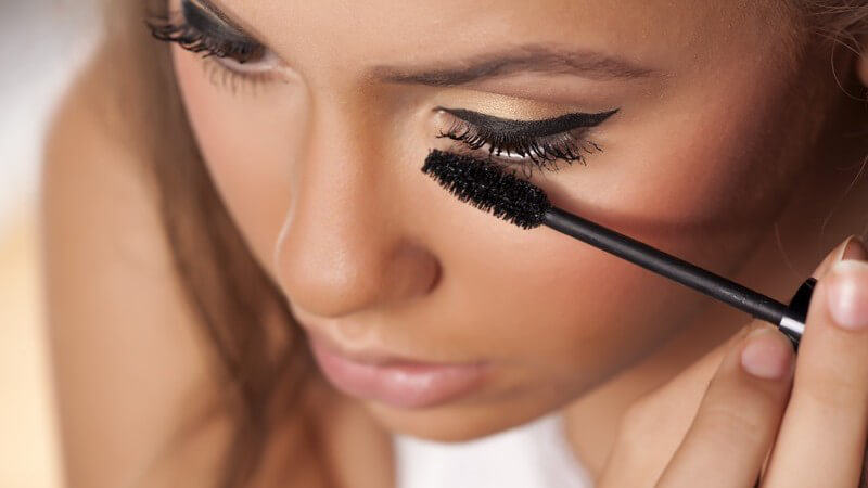 Frau mit dunklem Teint schminkt sich die Augenbrauen mit einem schwarzen Mascara
