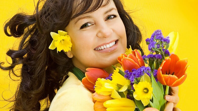 Lachende Frau hält bunten Blumenstrauß in Hand, gelber Hintergrund