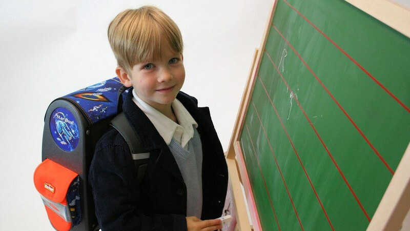 Kind mit Schulranzen steht vor einer Tafel