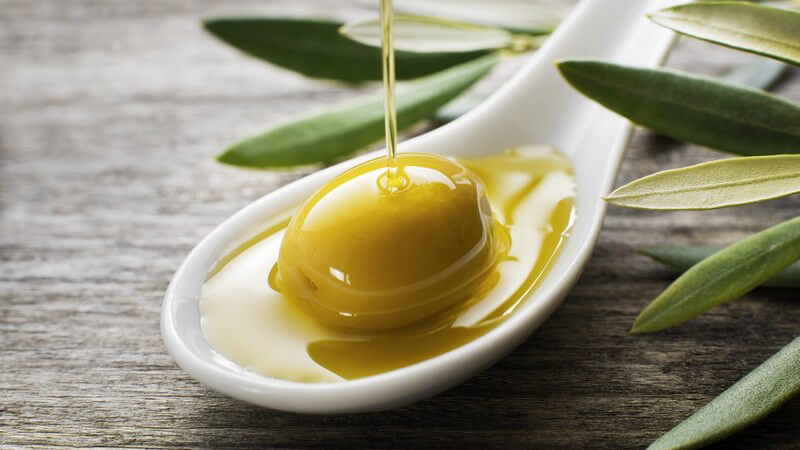 Olivenöl fließt auf eine grüne Olive auf einem weißen Löffel