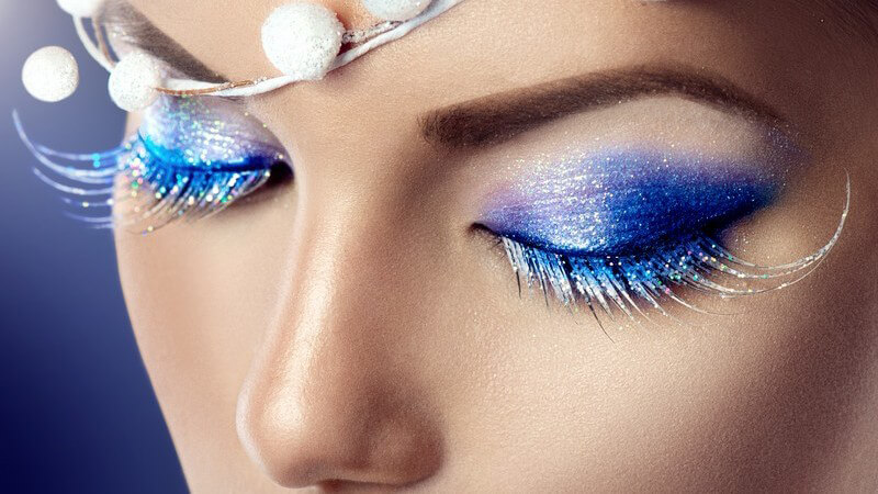 Nahaufnahme der Augenpartie einer Frau mit winterlich blau geschminkten Augen und Schnee-Schmuck auf der Stirn