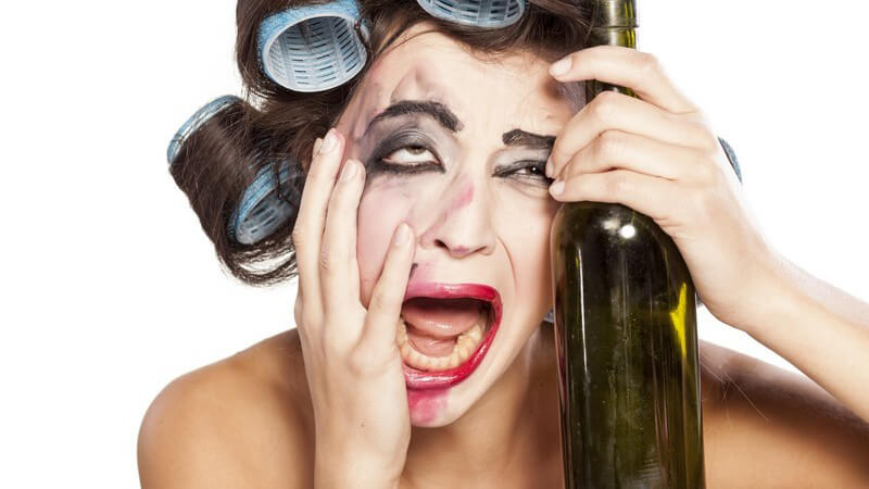 Betrunkene Frau mit verwischter Schminke und Lockenwicklern im Haar hält eine Weinflasche und schreit