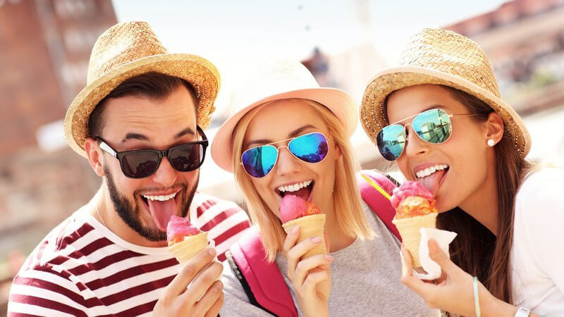 Drei Freunde mit Sonnenhut und Sonnenbrille essen ein pinkes Eis