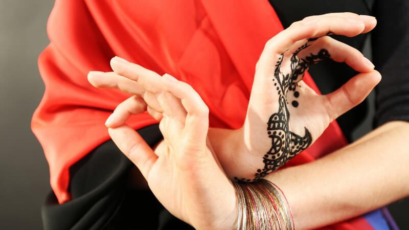 Frau in rotem Gewand hat ein Henna-Tattoo auf der einen und Armbänder an der anderen Hand
