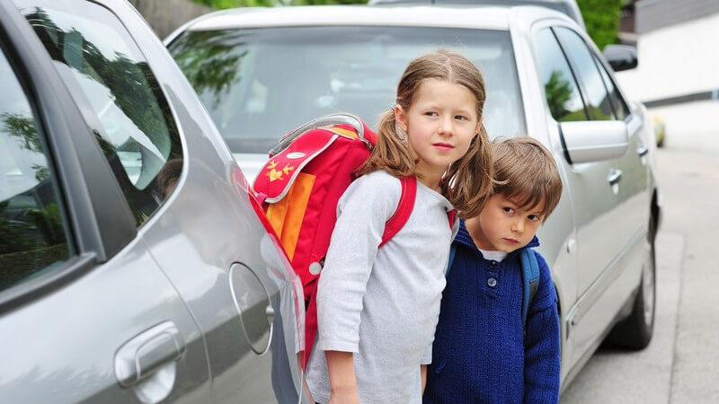 Zwei Kinder auf dem Schulweg, schauen ob Autos kommen, bevor sie Straße überqueren