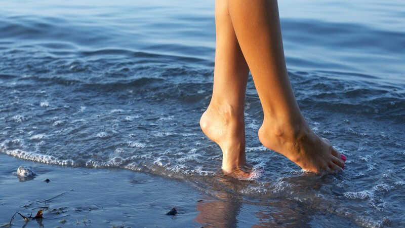 Frauenfüße laufen über den Strand am Meer