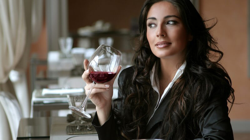 Frau sitzt mit Glas Rotwein im Restaurant und schaut zum Fenster raus