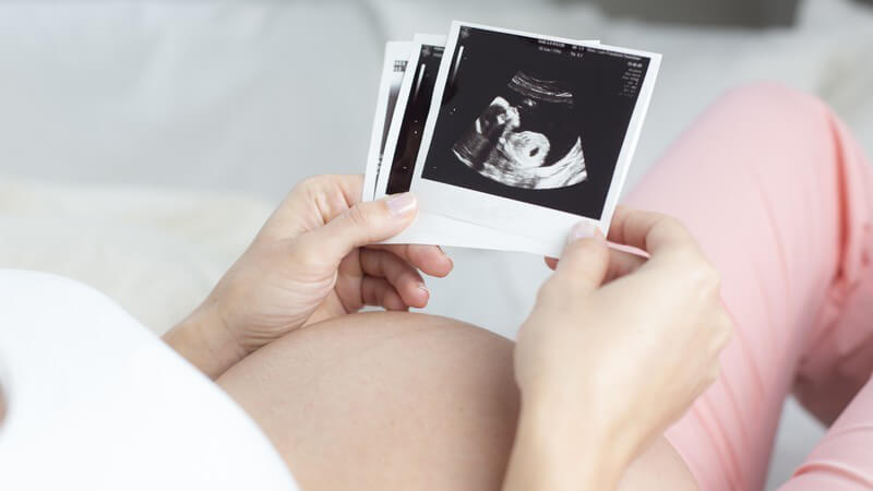 Schwangere Frau sieht sich Ultraschall-Fotos ihres Babys an