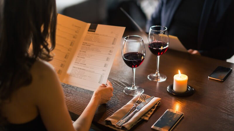 Paar sitzt bei einem Glas Rotwein am Tisch im Edelrestaurant und studiert die Speisekarte