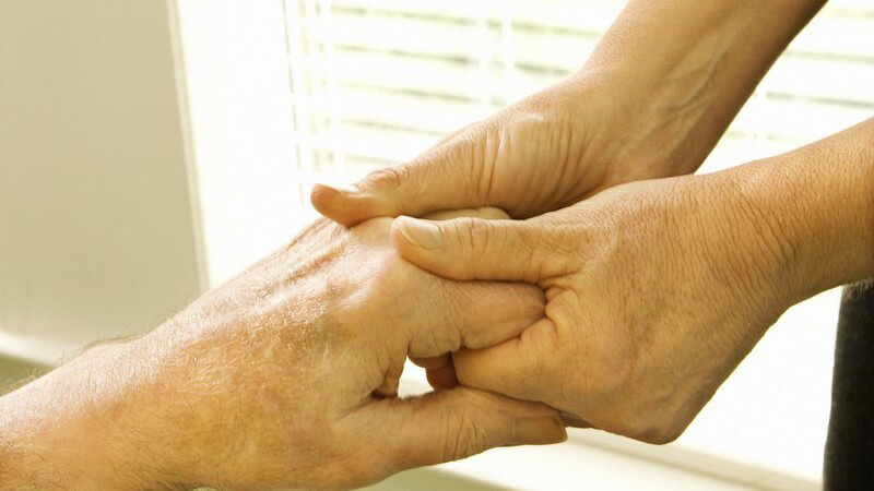 Nahaufnahme zwei Frauenhände massieren linke Hand eines älteren Mannes