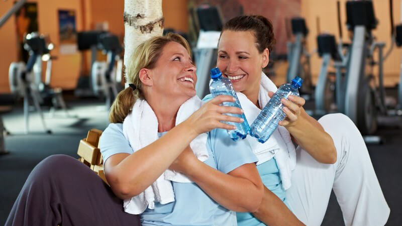 Zwei Frauen im Fitnessstudio machen Pause und stoßen mit Wasser an