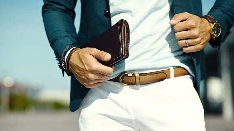 Geschäftsmann in blauem Sacko und braunem Gürtel auf weißer Hose, hält eine Geldbörse in der Hand