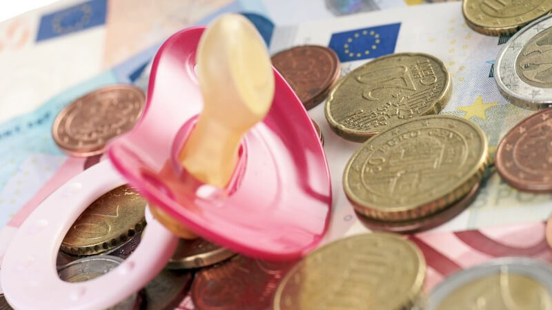Pinker Babyschnuller liegt auf Euro-Geldscheinen und -Münzen