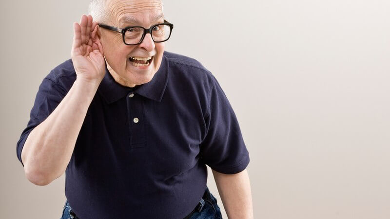 Älterer Mann hält Hand hinters Ohr weil er nicht hört