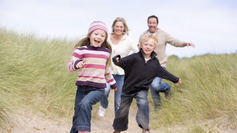 Paar mit zwei Kindern, Familie rennt lachend Strand entlang