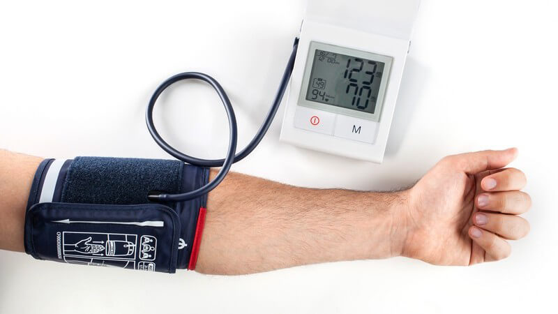 Ausgestreckter Arm mit Manchette und Blutdruckmessgerät vor weißem Hintergrund