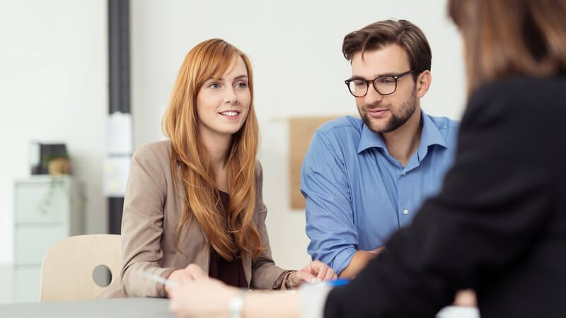 Junge rothaarige Geschäftsfrau und Mann in blauem Hemd in einem Gespräch mit einer Beraterin